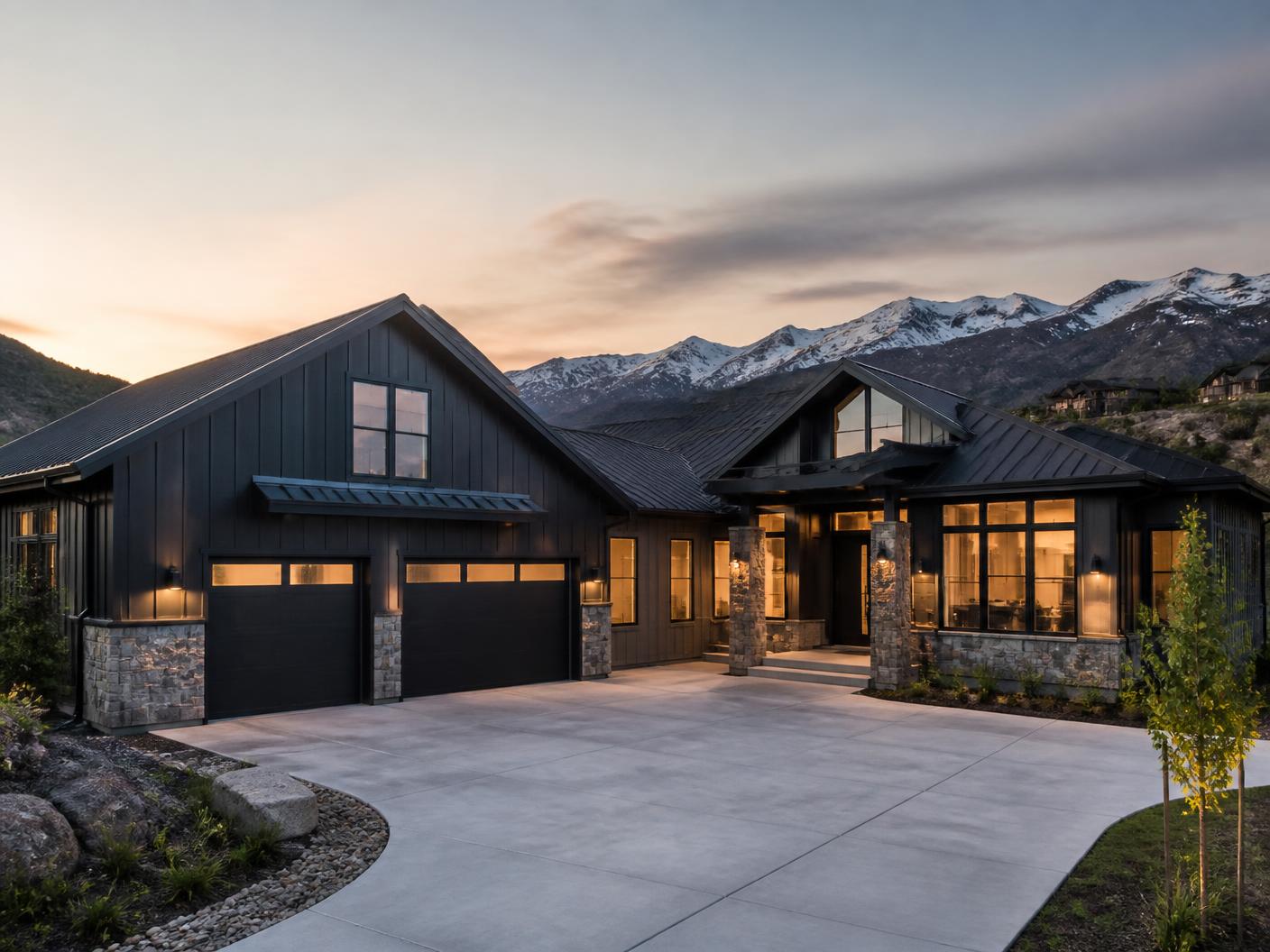 Completed dark board-and-batten mountain modern home with stone base at dusk